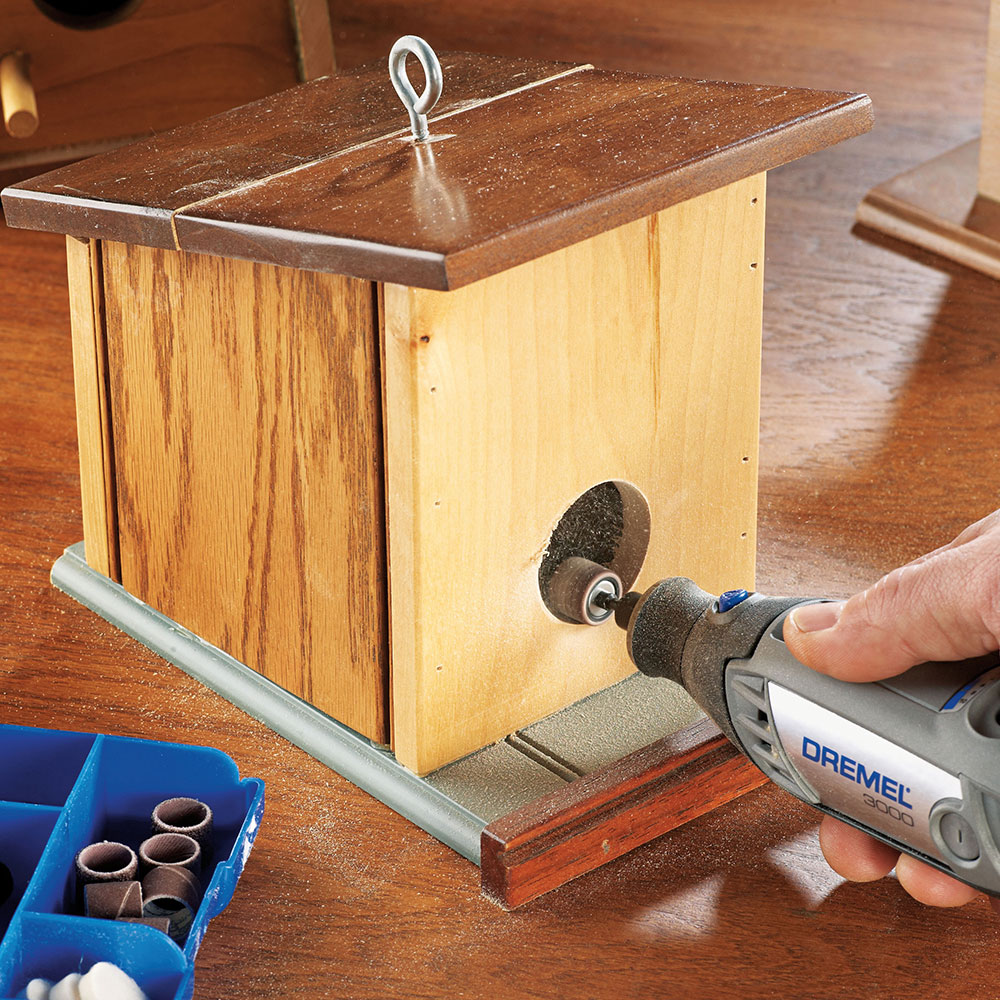 A rotary tool sands the entrance hole of a DIY wooden bird feeder.