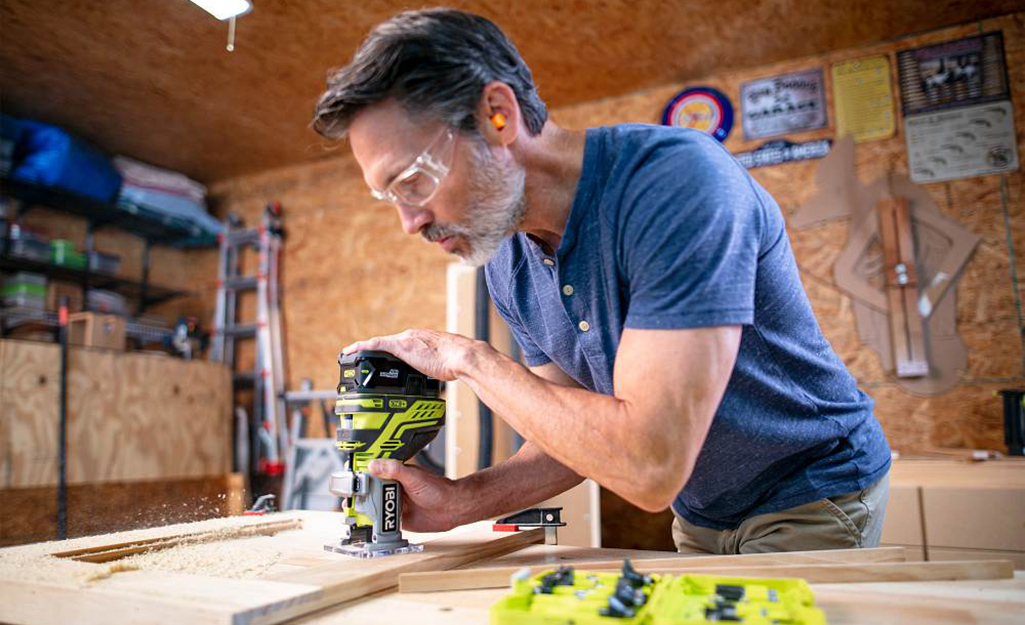 A person uses a handheld router in a wood workshop.