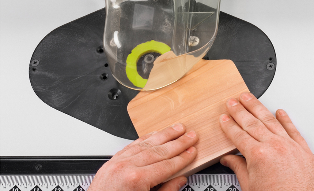 A person uses a tabletop router to get a clean and rounded edge on a piece of wood.