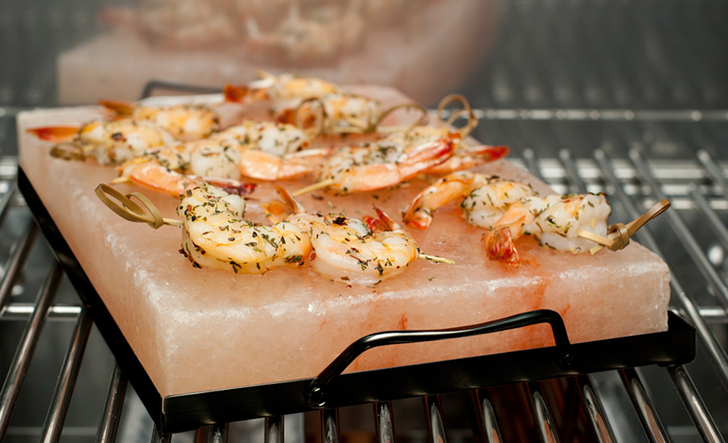 Shrimp lay on top of a salt rock on top of a metal tray in an oven.