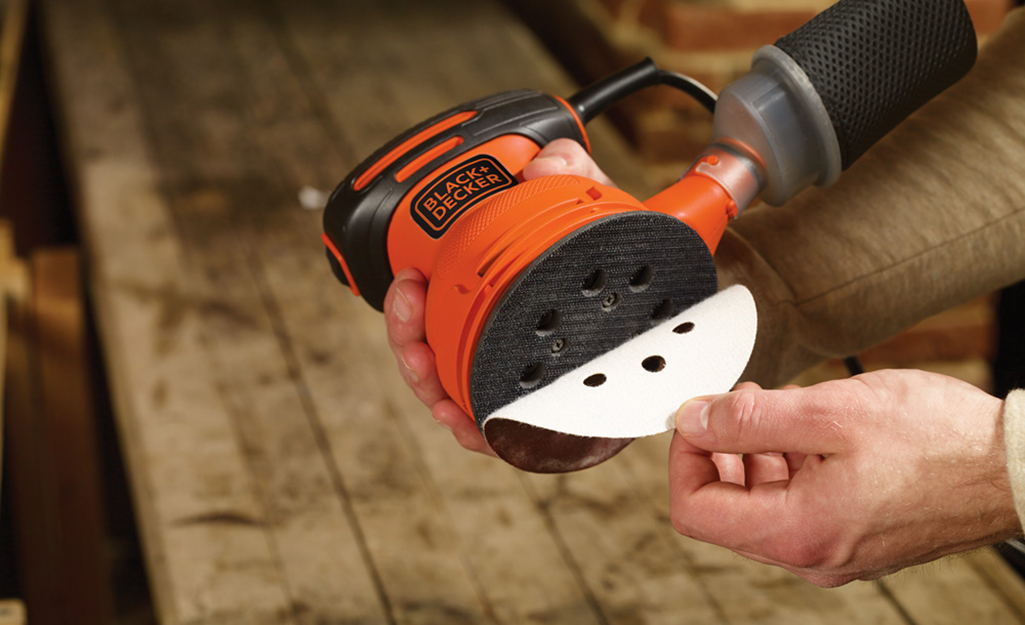 A person removes a piece of sandpaper from the sanding pad of a random orbital sander.