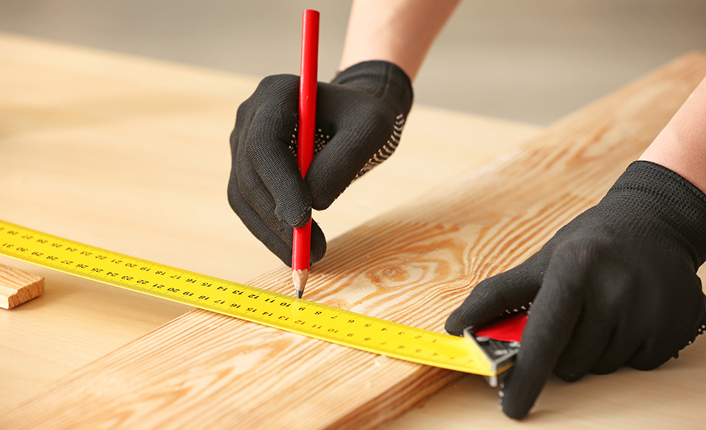 A person uses a measuring tape and a pencil to mark a board.