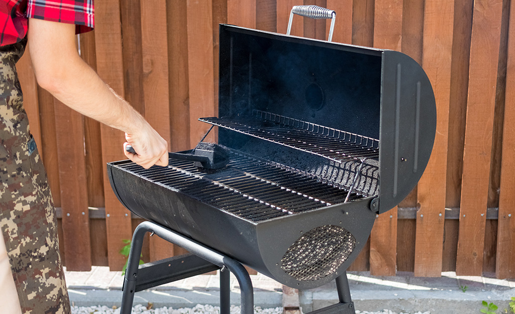 Someone cleaning the grill grates on a smoker.