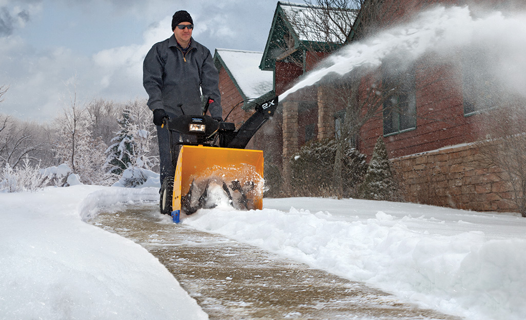 A person using a snow blower to clear snow from a sidewalk.