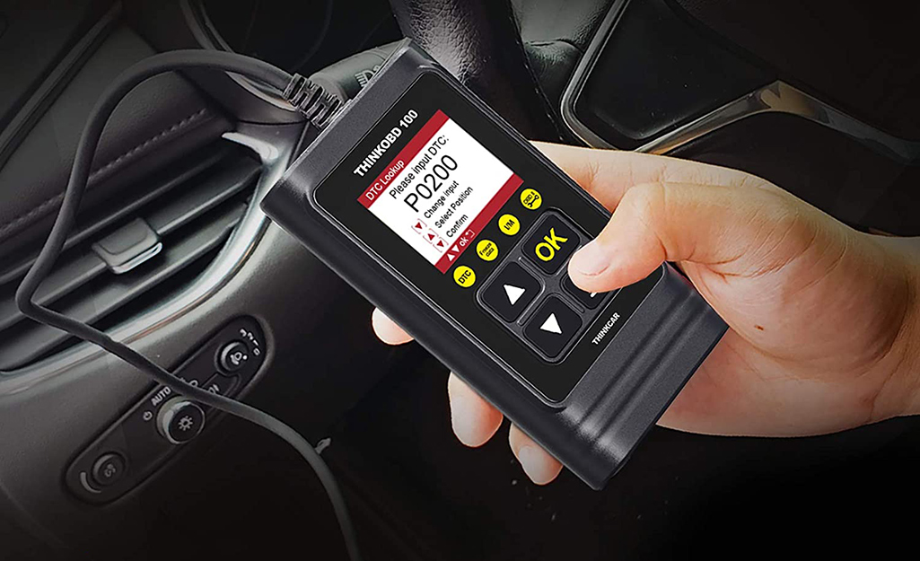 A person pressing buttons on an OBD2 scanner connected to a vehicle.