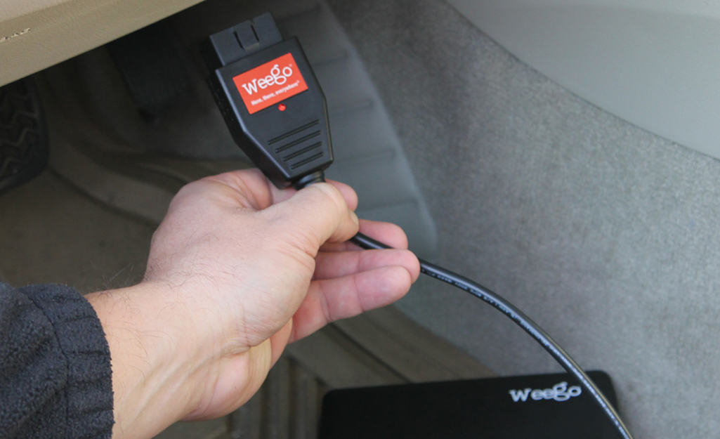 a hand connecting an OBD2 scanner to a vehicle