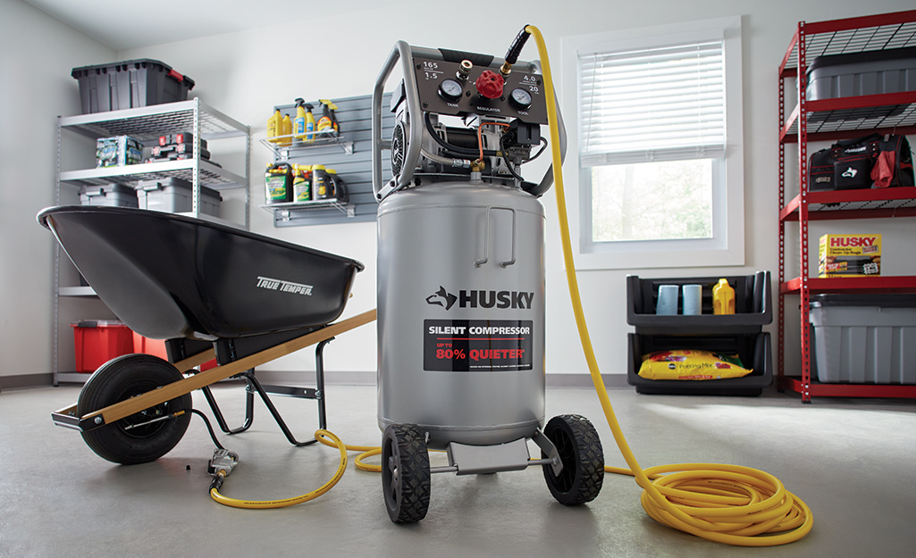 An air compressor in a garage with a long yellow air hose.