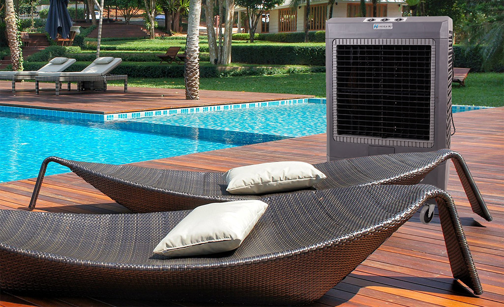 An evaporative cooler stands next to two lounge chairs alongside a pool.