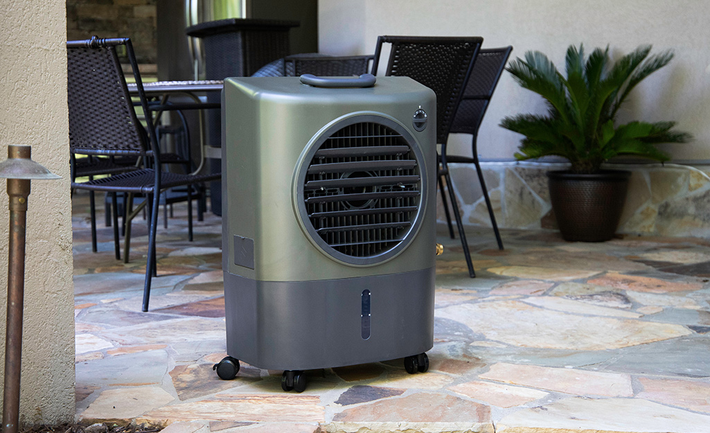 An evaporative cooler stands on a stone patio and in front of an outdoor dining table.