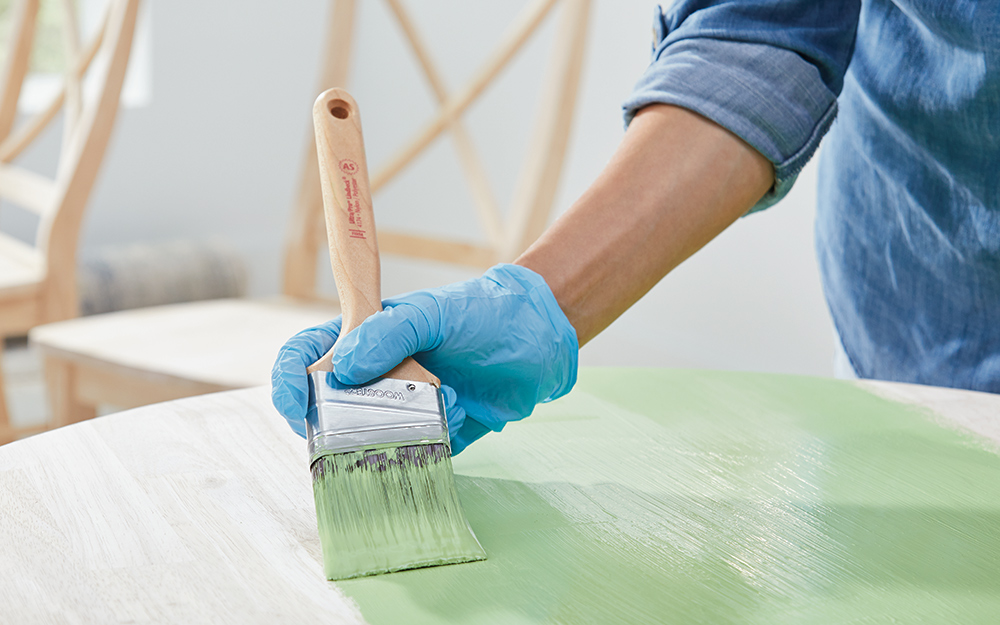 A person uses a brush to apply green chalk paint to a table.