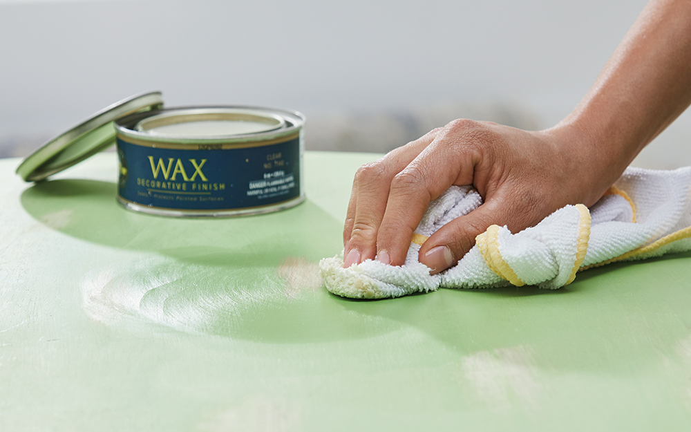  A person applies furniture wax to a table painted with chalk paint.