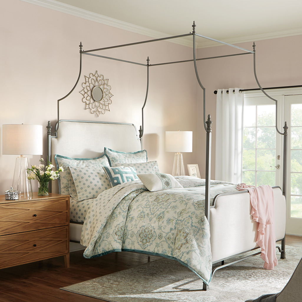 A white, light blue and brown medallion comforter with matching bedding dresses up a wrought iron canopy bed.