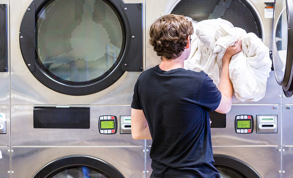 A person putting a comforter in a washing machine.