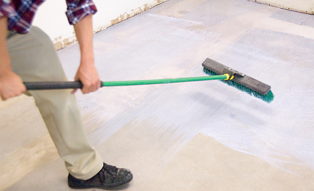 A person applies primer to a floor with a push broom.