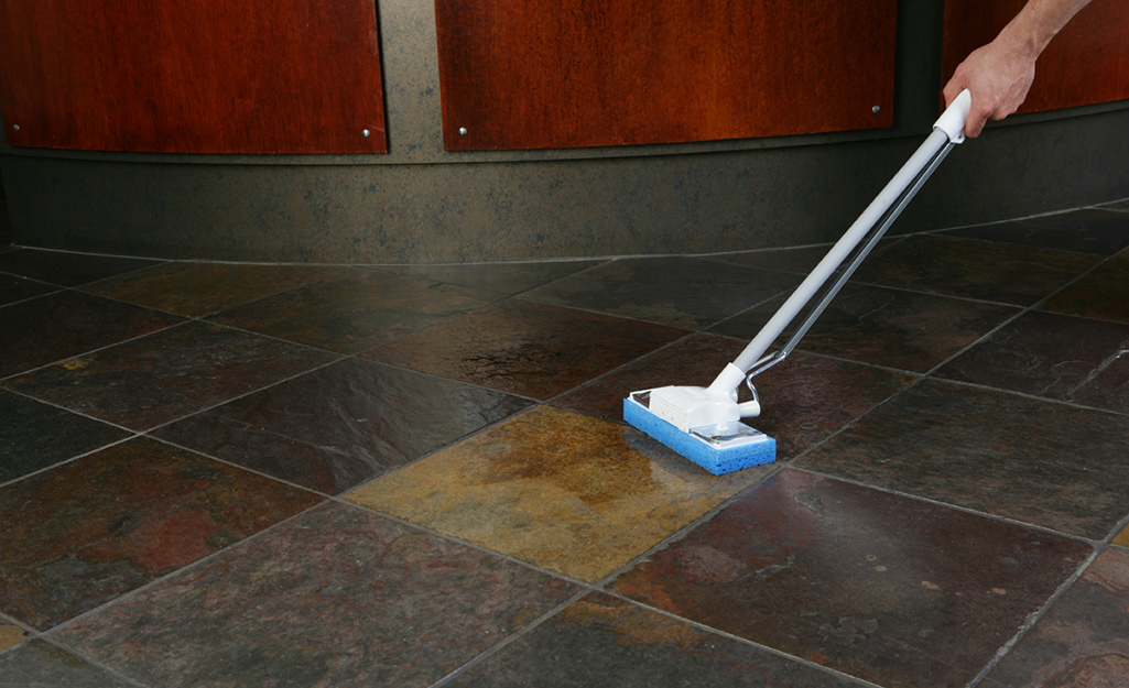 A person uses a sponge mop to apply a layer of waterproofing agent to a concrete floor.