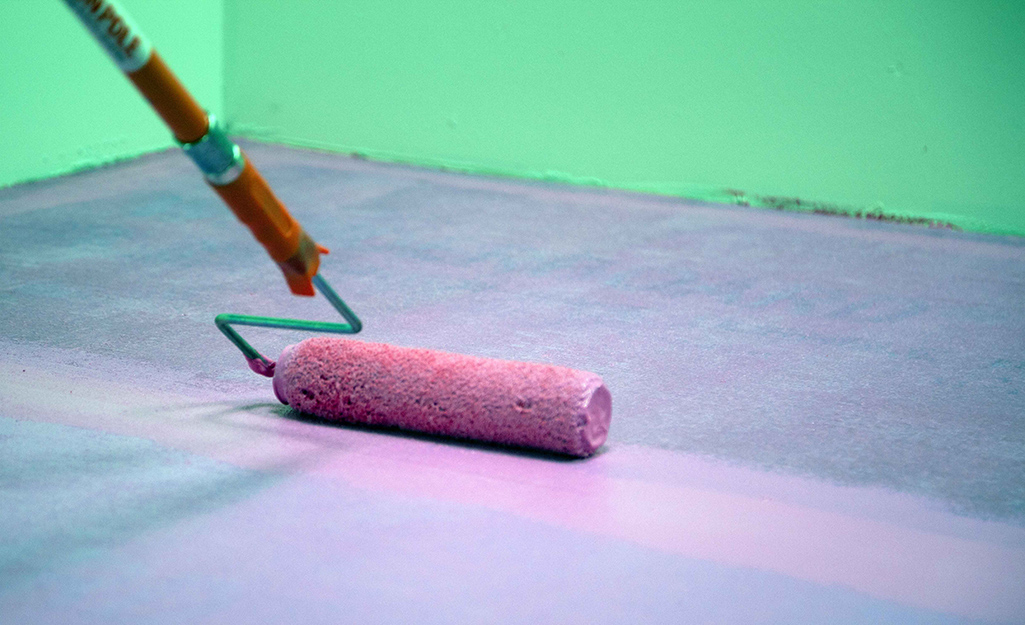 A paint roller applies waterproofing agent over a layer of waterproofing membrane on the floor.