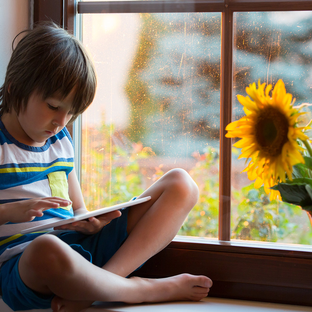 Child sitting beside a window with a sunflower outside.