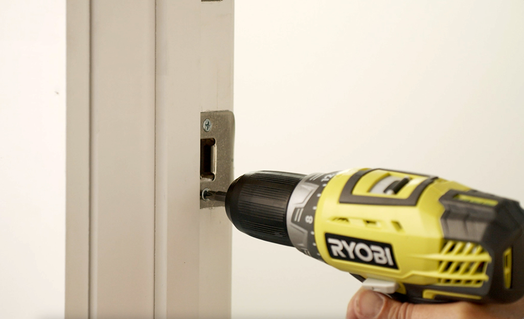 A person tightening screws and adjusting strike plates so the door will close and latch tightly.