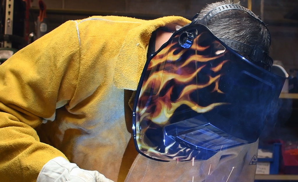 A person wearing special welding safety gear, such as a helmet, jacket and gloves. A person wearing special welding safety gear, such as a helmet, jacket and gloves.