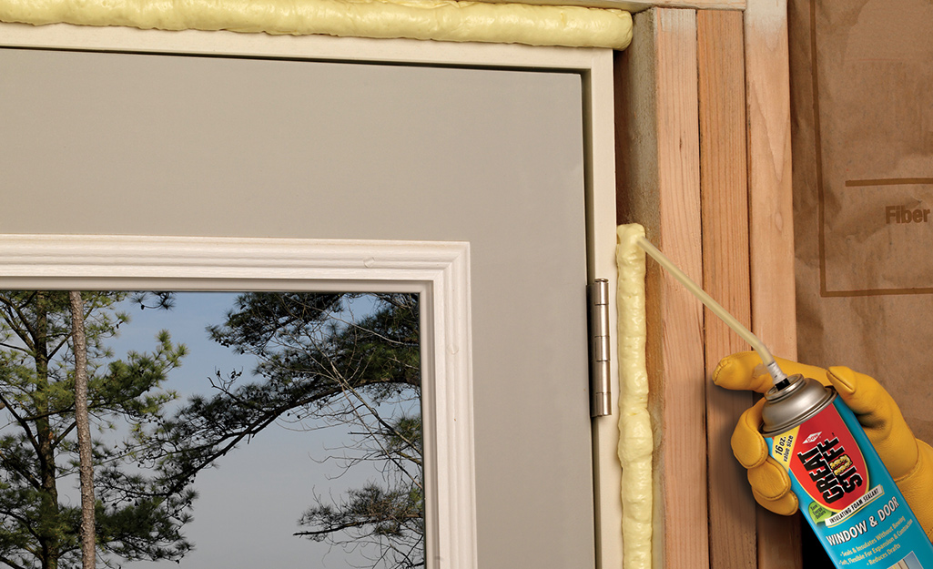 A person spraying foam insulation along the edge of a door.