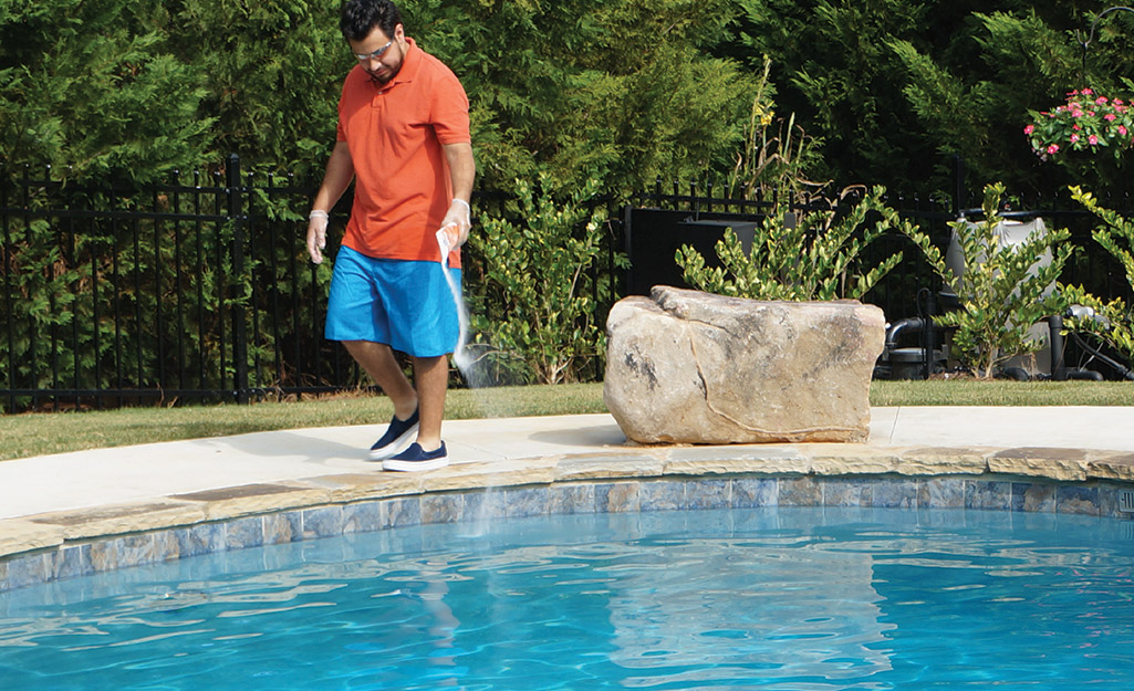 A person adding pool shock to an in-ground pool.