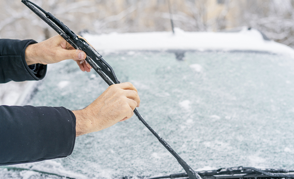 A person holds up the windshield wiper of a car with an ice-covered windshield.