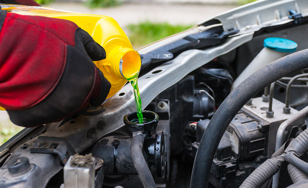 A person wearing red gloves adds coolant to a vehicle.