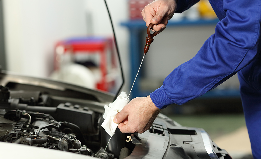 A person wipes off a vehicle's engine oil dipstick. 