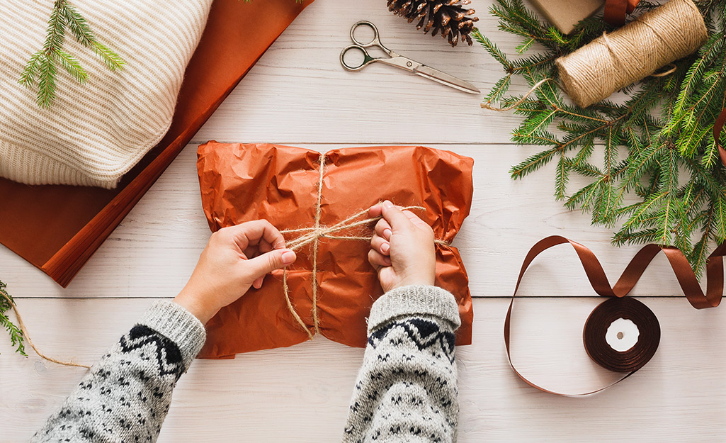 A person tying twine around a parcel wrapped with red paper.