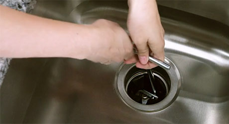 A person uses an Allen wrench to rotate a garbage disposal's blades.