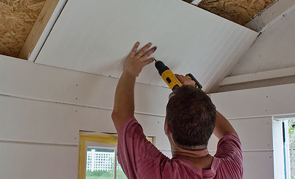 A person attaches a board to the ceiling of she shed.