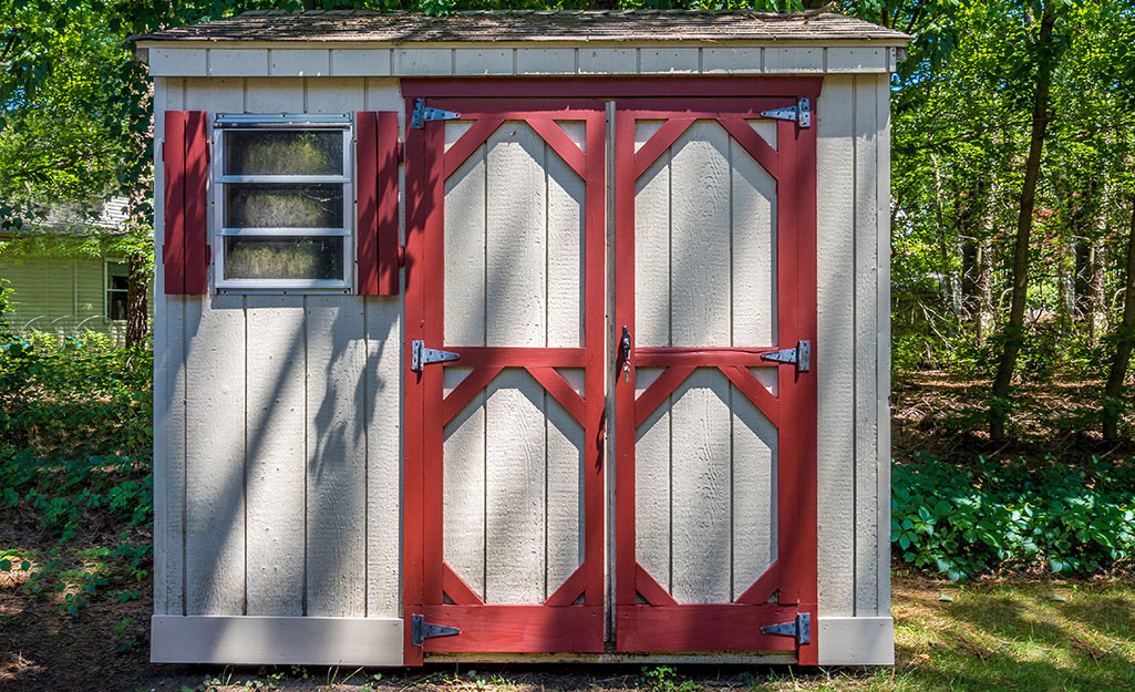 Doors outlined in barn red accent a small gray she shed.