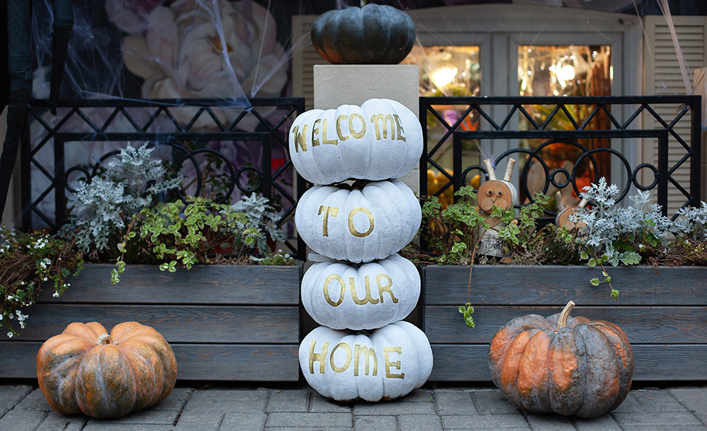 Gold paint on a stack of white pumpkins reads welcome to our home.