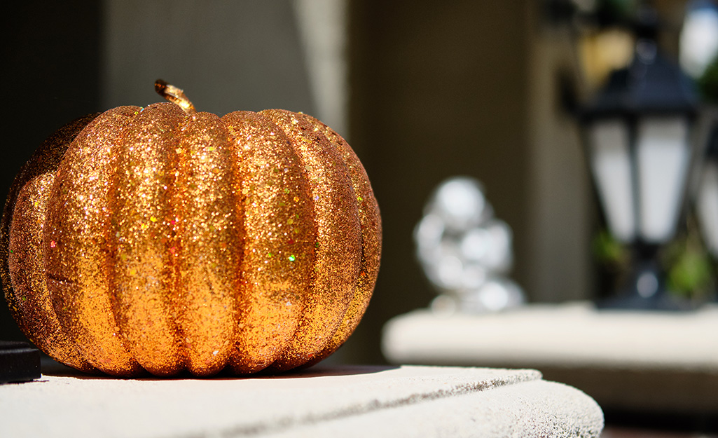 A layer of shiny glitter covers an orange pumpkin sitting outside.