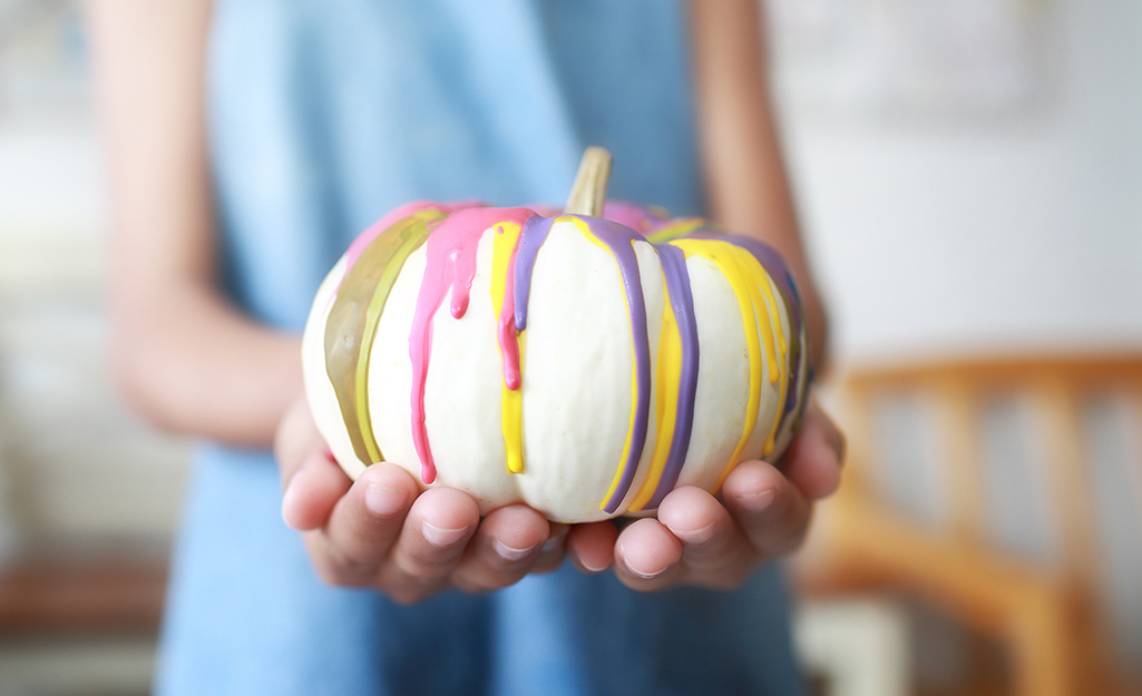 A person holds a white pumpkins decorated in dripped crayon wax.