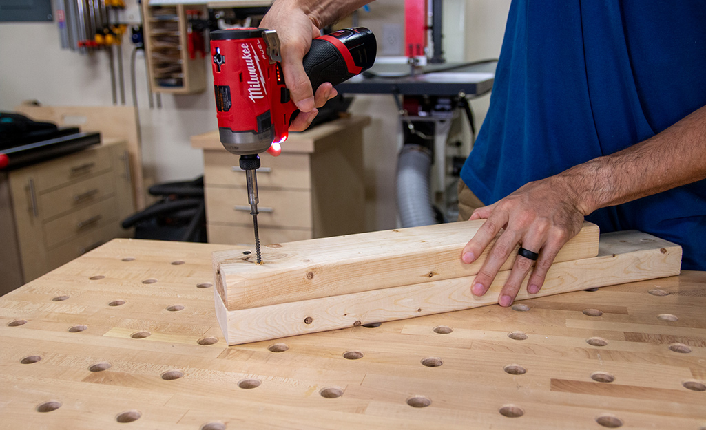 A person using an impact driver on two pieces of plywood.