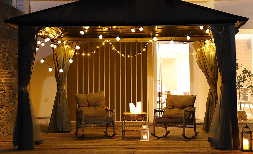 String lights, candles and a lantern provide warm lighting under a pergola at night.
