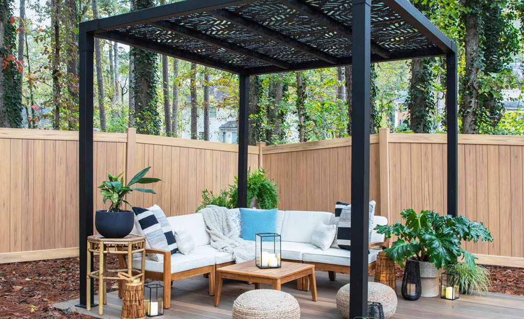 Outdoor furniture sits under a pergola in front of a privacy fence.