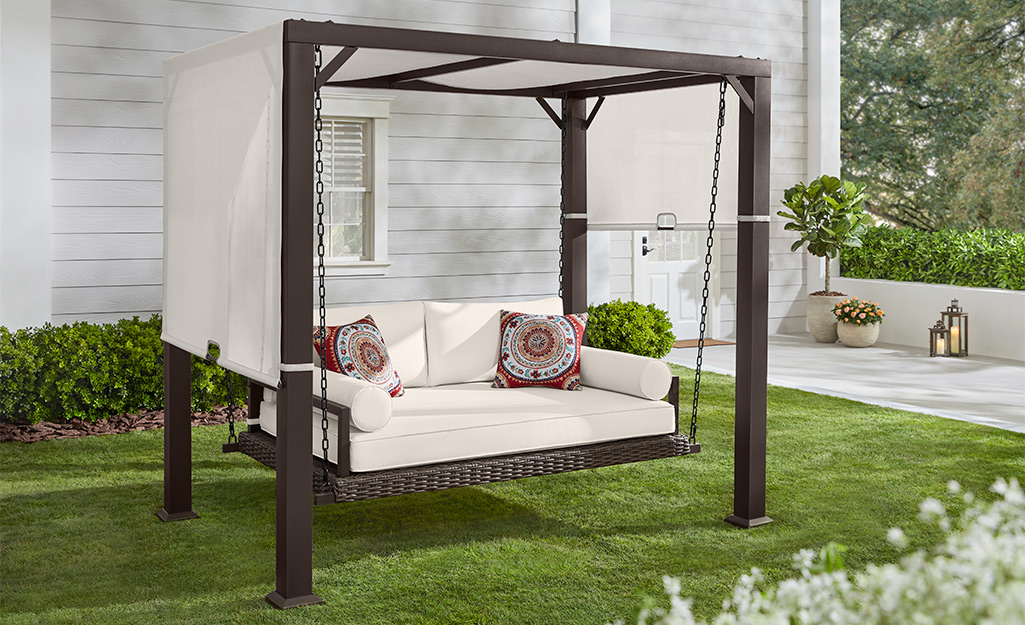 A canopy over a pergola provides shade for a swing with white cushions.