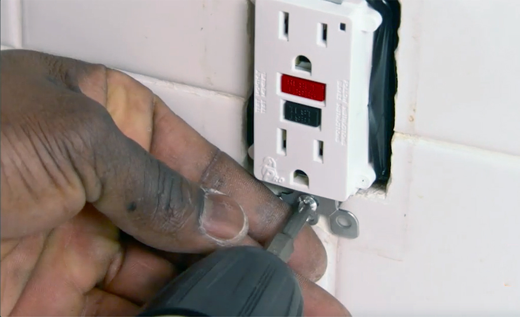 A person tightens the mounting screws of a GFCI outlet.