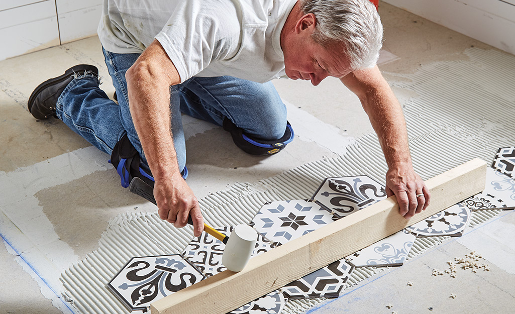 Man leveling rows of tile using a mallet and wood board.