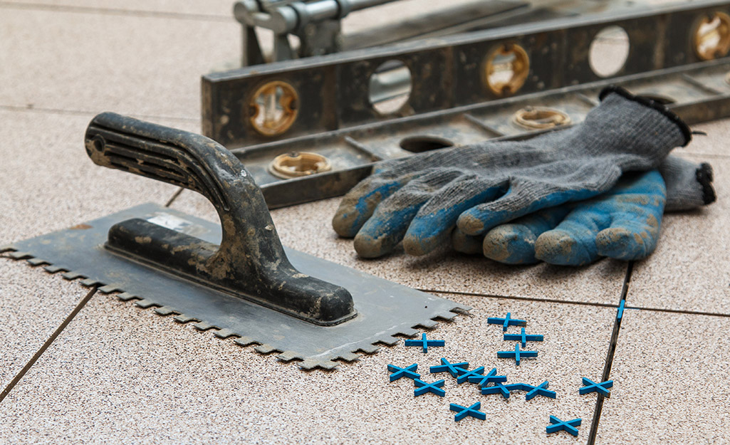 A trowel, spacers and level placed next to work gloves.