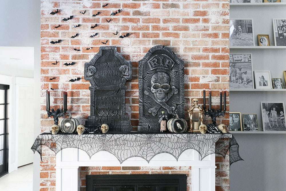 A fireplace mantel decorated for Halloween with headstones, candlesticks, and skulls.