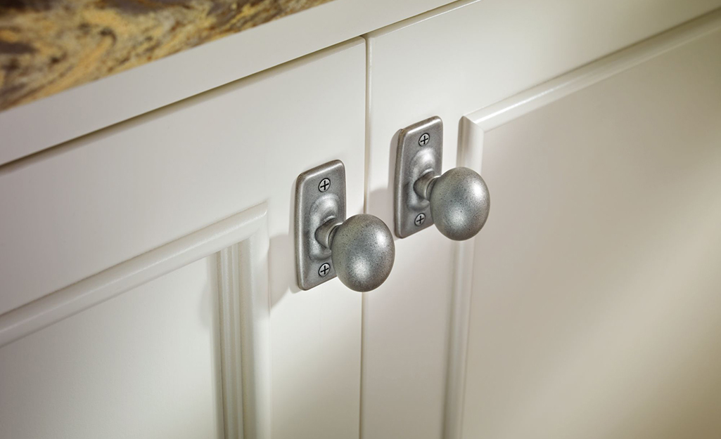 Nickel cabinet knobs with backplates installed on white cabinet doors.
