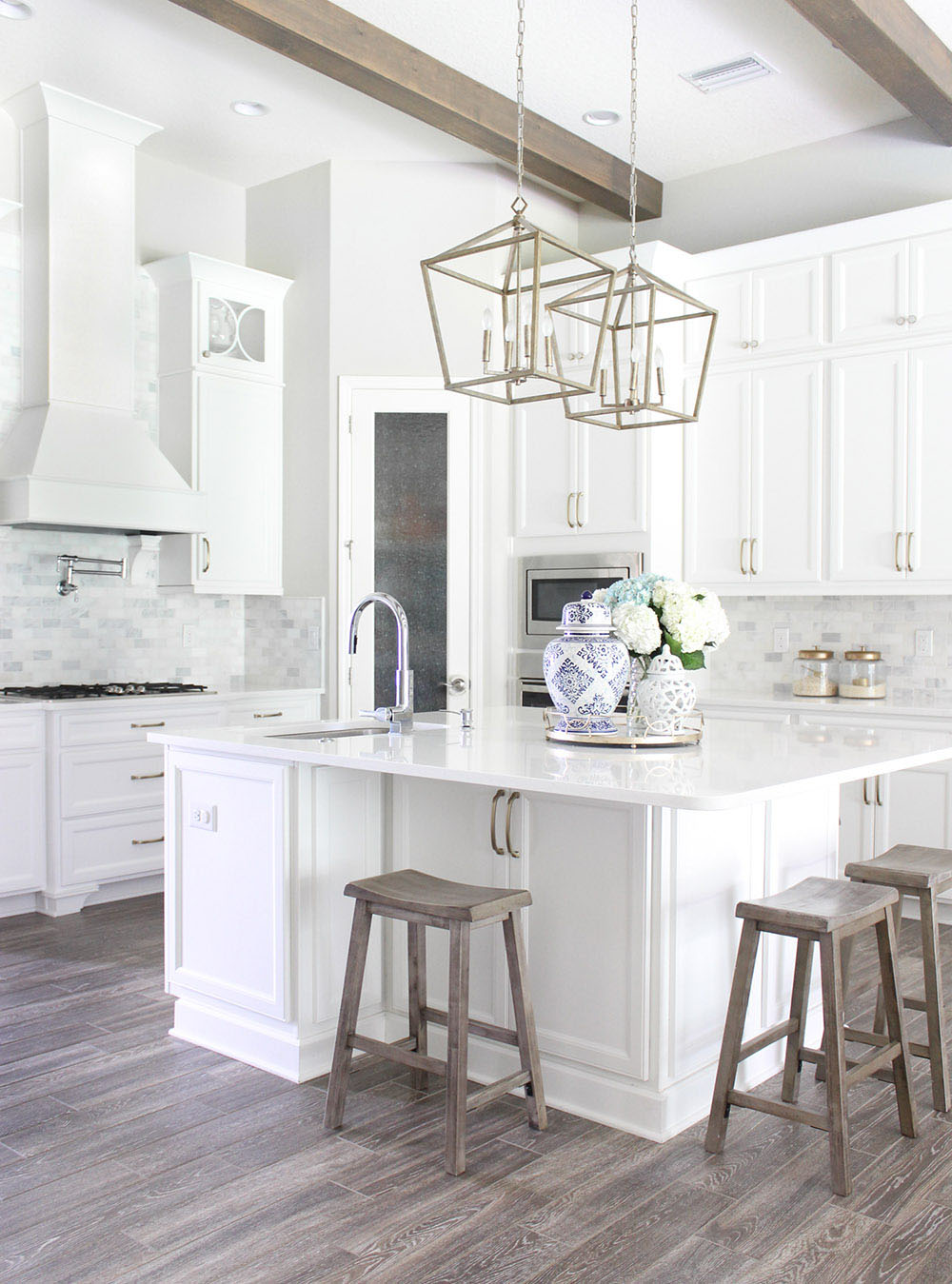 An updated white kitchen with wood beams on the ceilings.