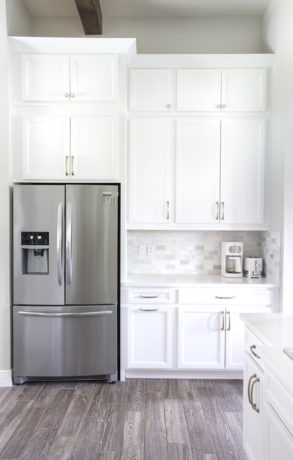 A stainless steel refrigerator sits below a wall of stacked white cabinets.