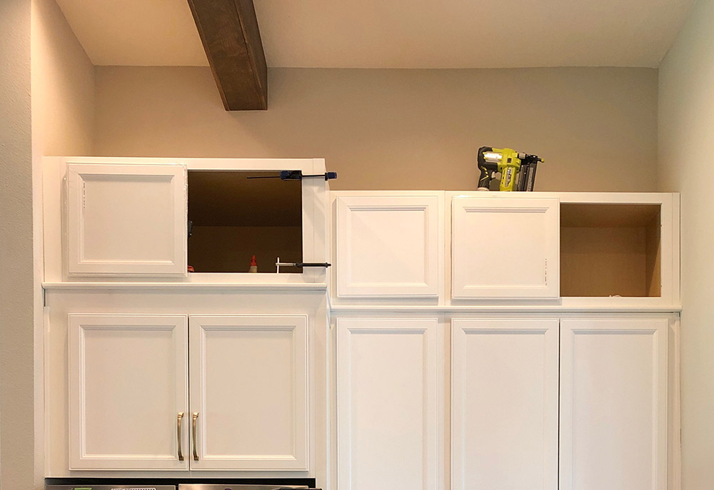 An upper row of white cabinets installed on top of current kitchen cabinets.