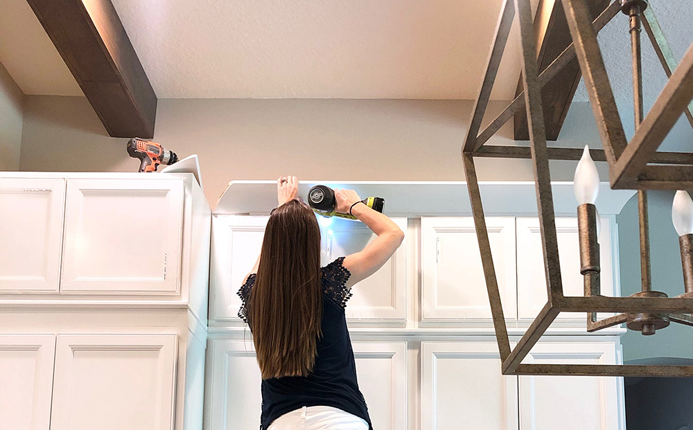 A woman installs crown moulding to newly installed cabinets.