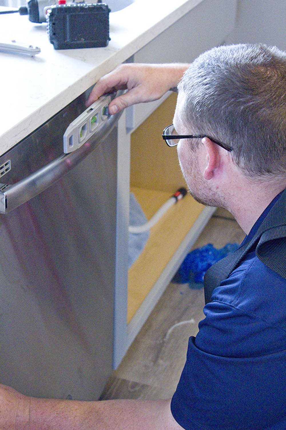 A man installing and leveling a dishwasher inside a home.