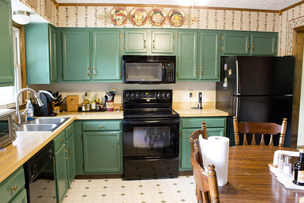 A kitchen with green cabinets, wood countertops, and black appliances.